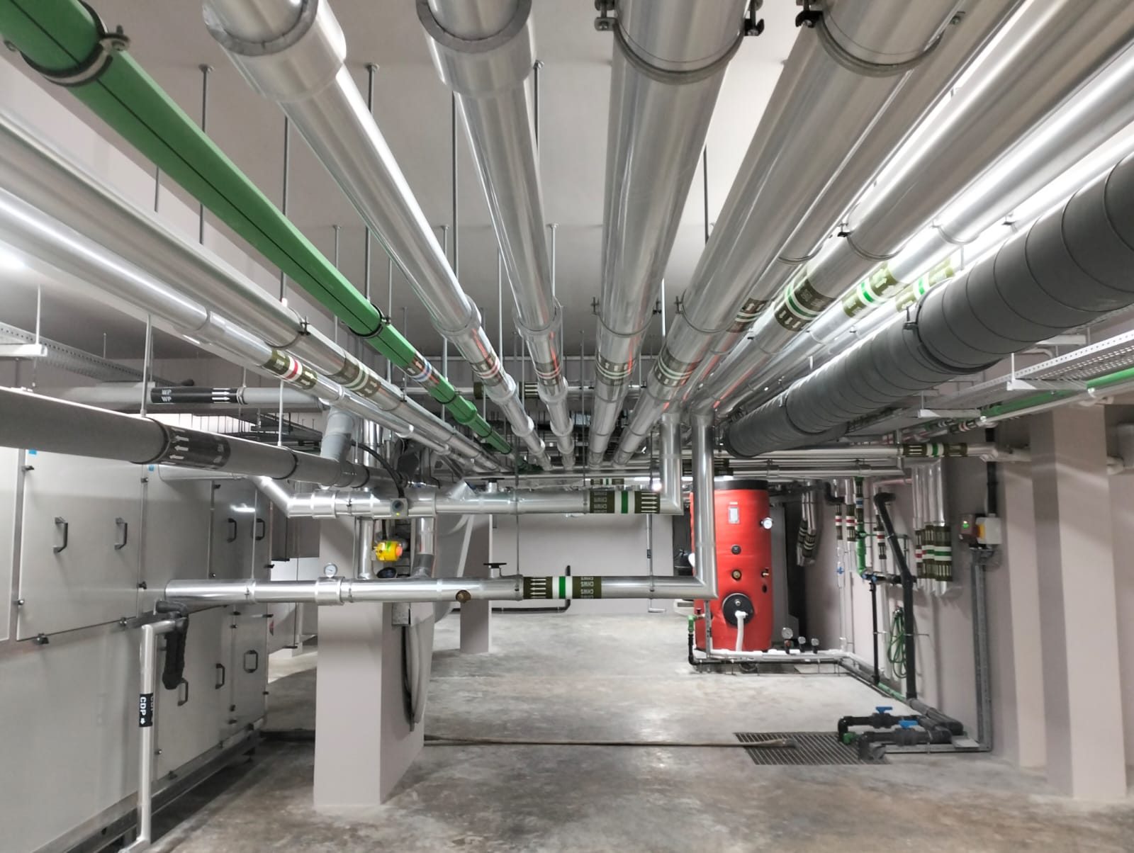 Plant room ceiling with dense runs of insulated chilled water piping, spiral ductwork and air handling units